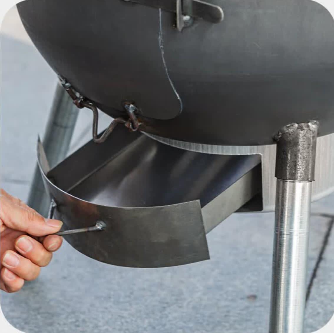 Person using a tool to open a black barbecue grill lid.